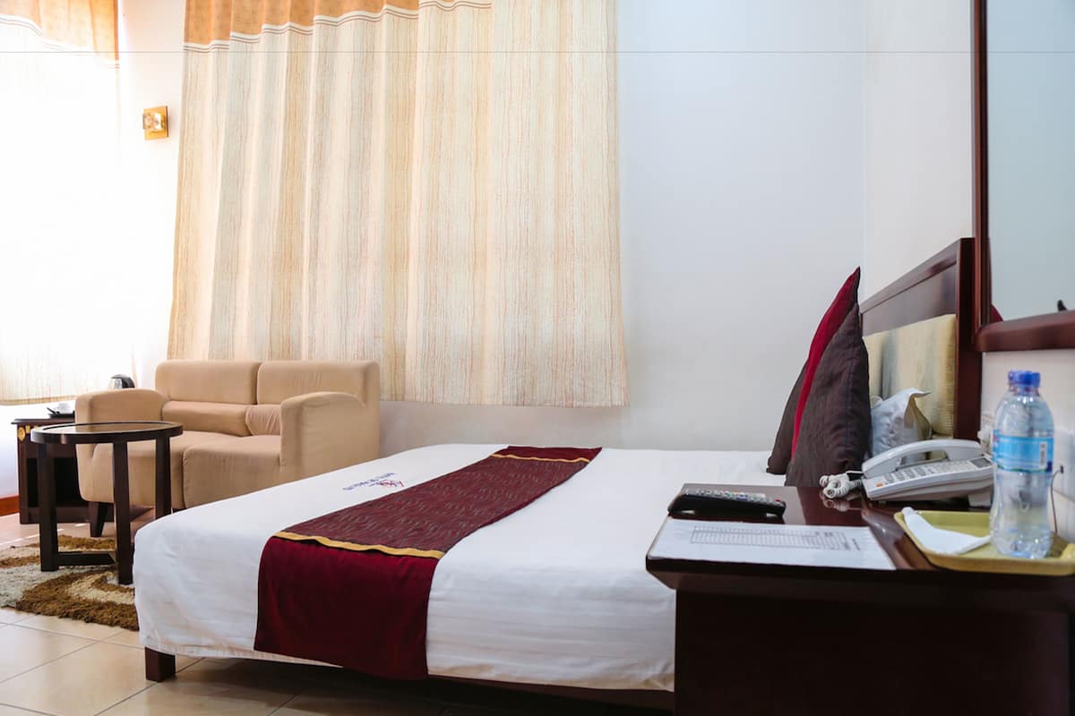 Une chambre d’hôtel avec un lit, un bureau doté d’un téléphone et d’une bouteille d’eau, une chaise et une petite table.