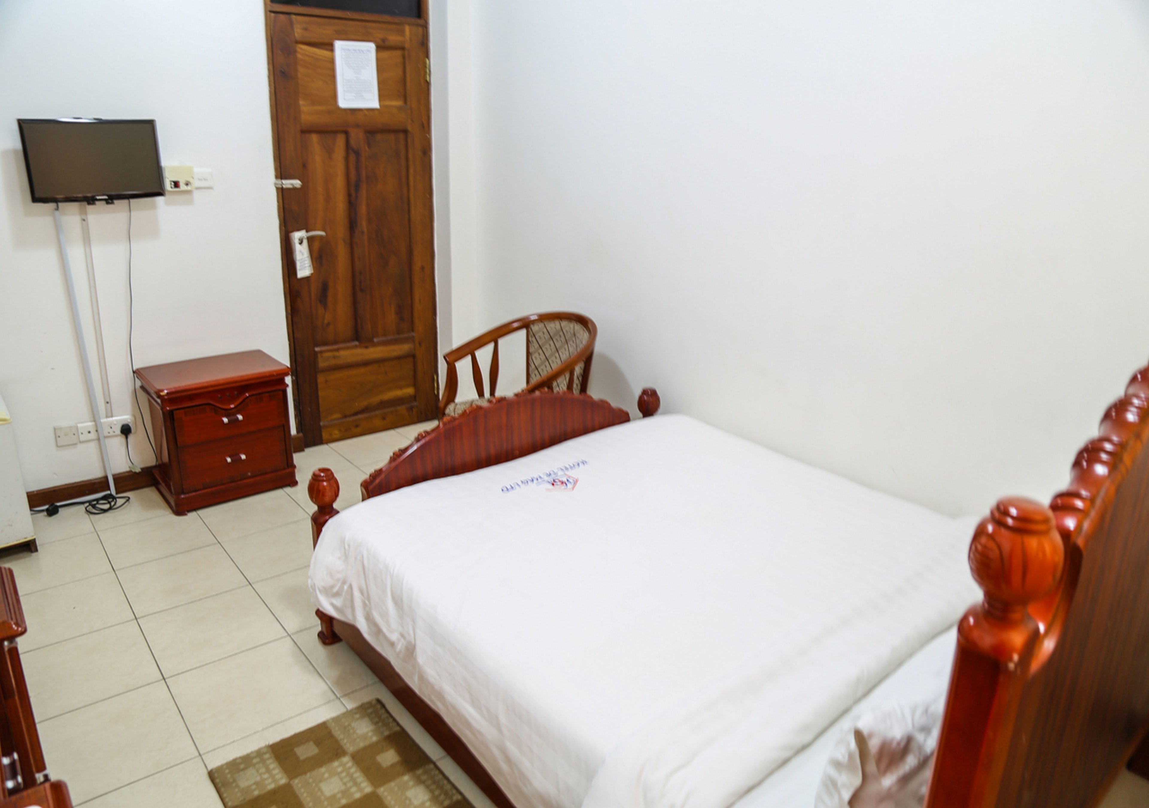 A bedroom with a wooden bed, a wooden nightstand, a television on a stand, and a wooden door.