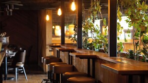 A restaurant interior with wooden tables and bar stools, hanging light bulbs, and potted plants. - Sherwood Queenstown (Queenstown)