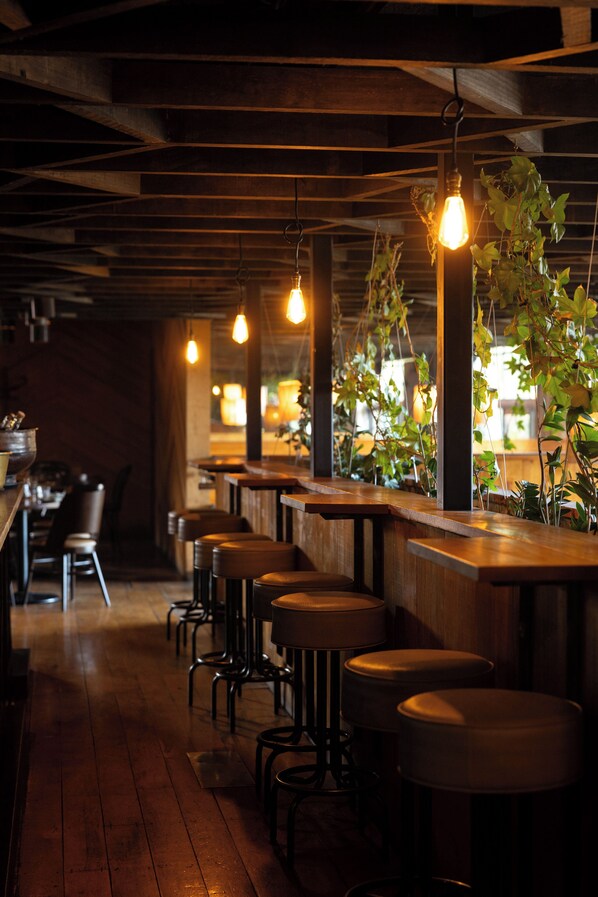L’intérieur d’un restaurant avec des tables en bois, des tabourets de bar, des ampoules suspendues et des plantes en pot.