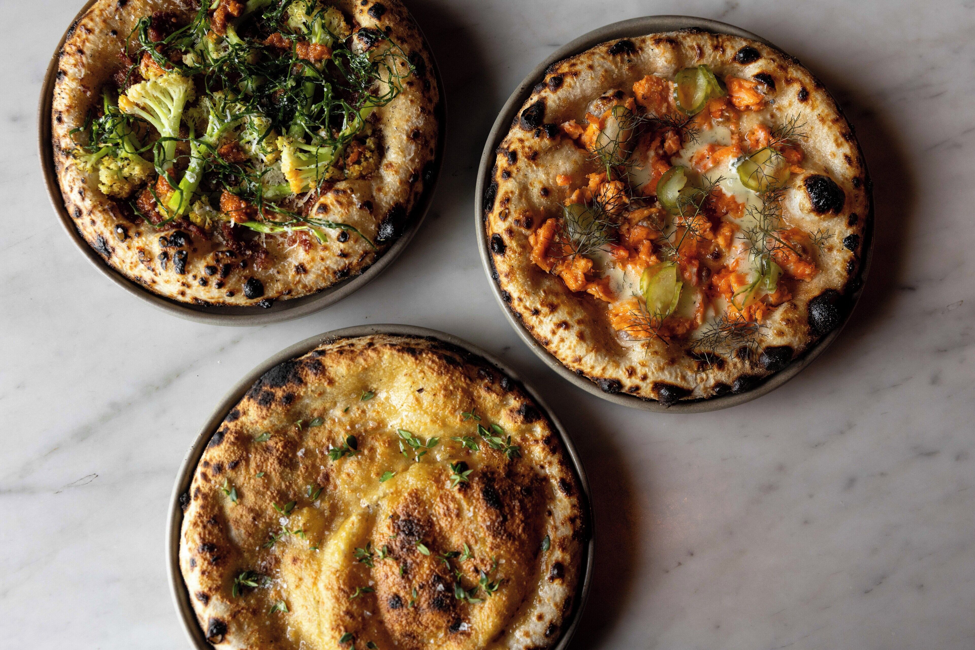 Three pizzas with different toppings on a marble surface.
