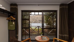 A room with a view of a lake, a table with books, and a hanging garment bag. - Sherwood Queenstown (Queenstown)