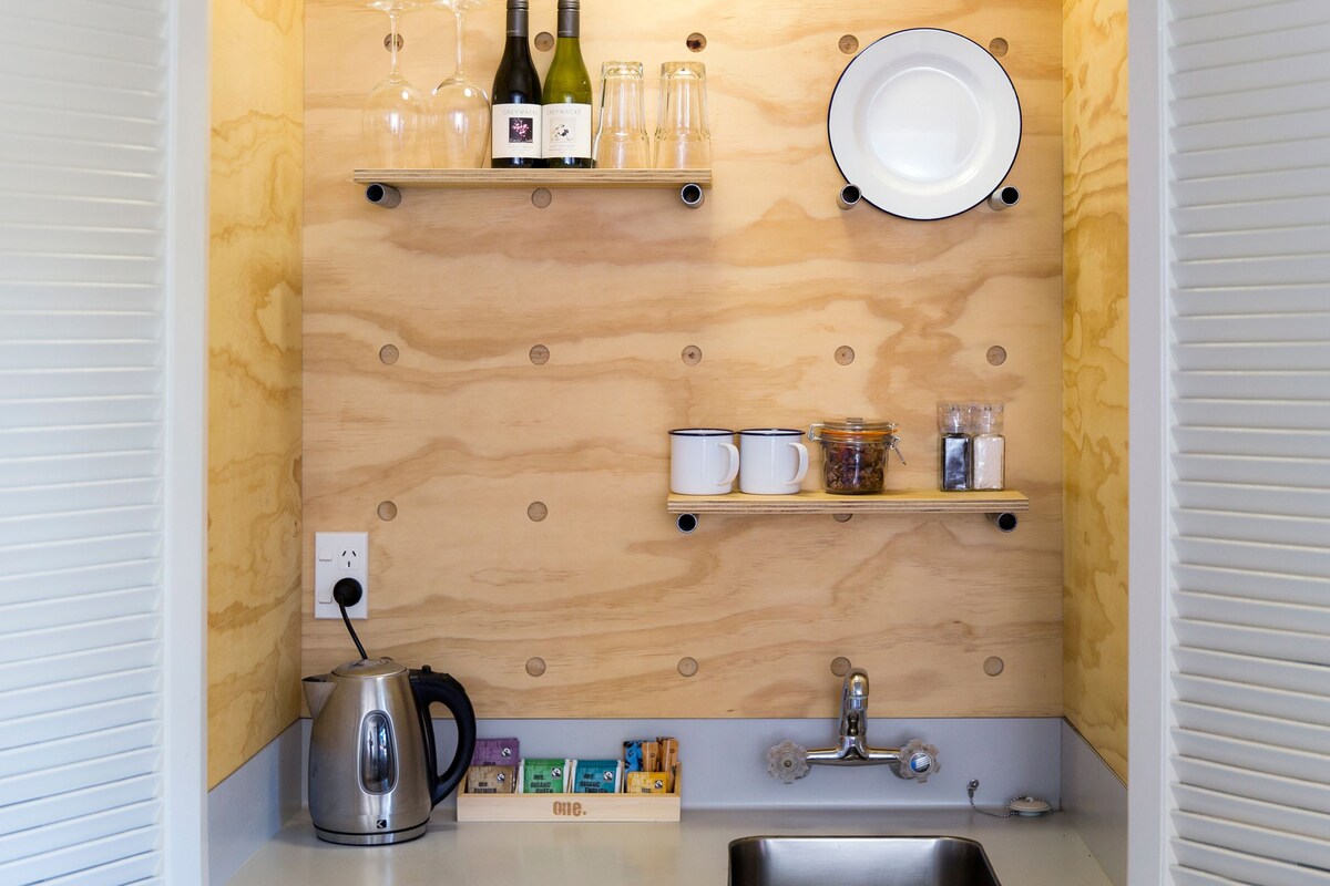 Une cuisine compacte dotée de meubles en bois, d’un évier en acier inoxydable, d’une bouilloire et de divers ustensiles de cuisine.