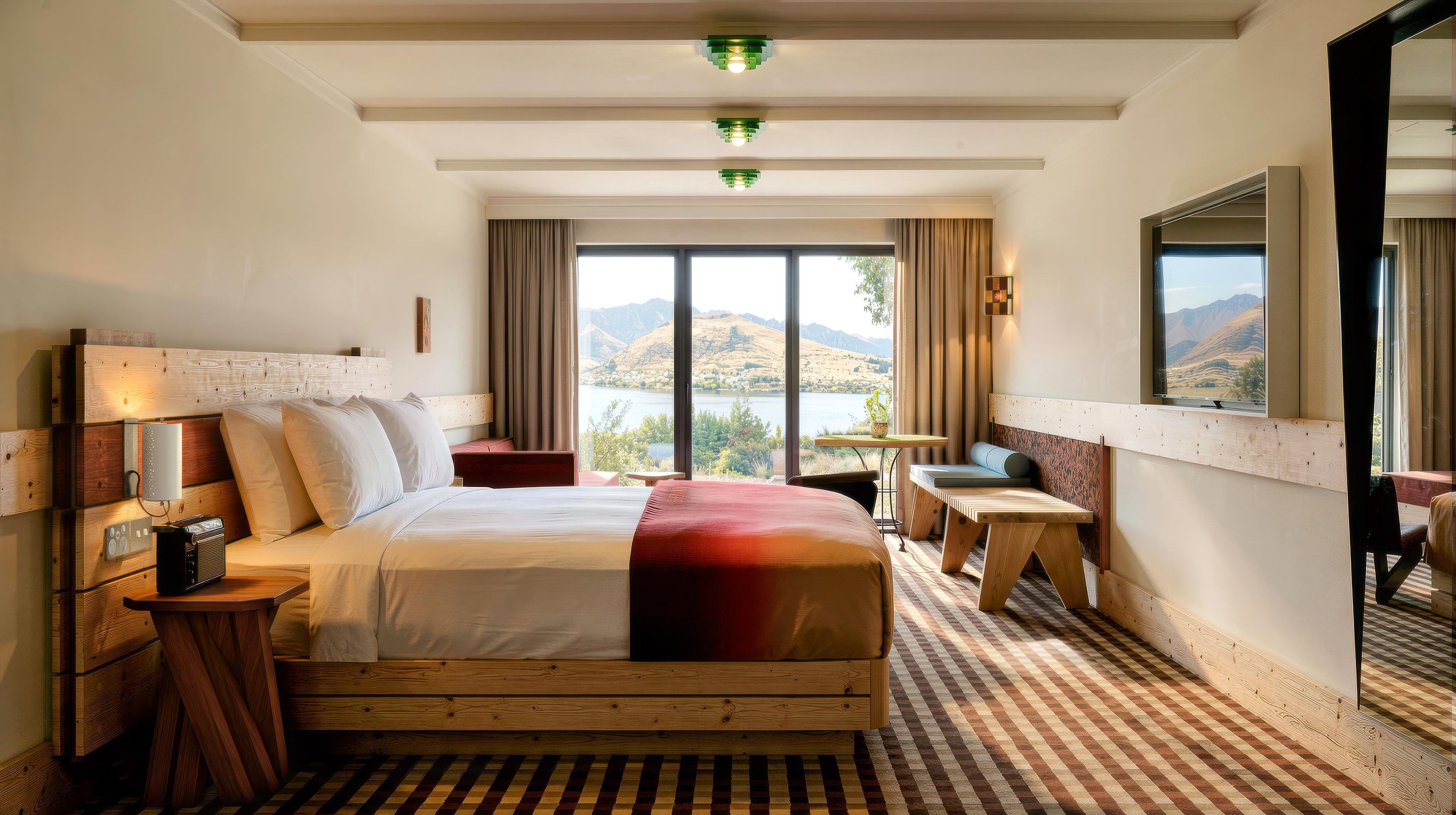 A hotel room with a large bed, a desk, a chair, and a view of the mountains.
