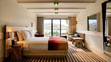 A hotel room with a large bed, a desk, a chair, and a view of the mountains.