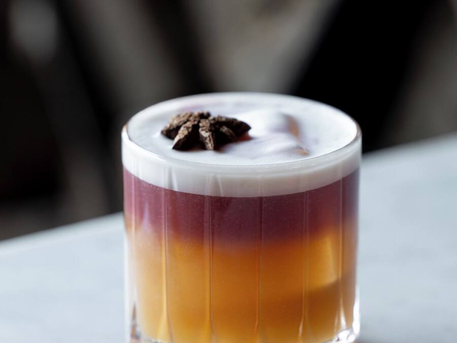 Bebida en capas en un vaso transparente, adornada con chocolate.