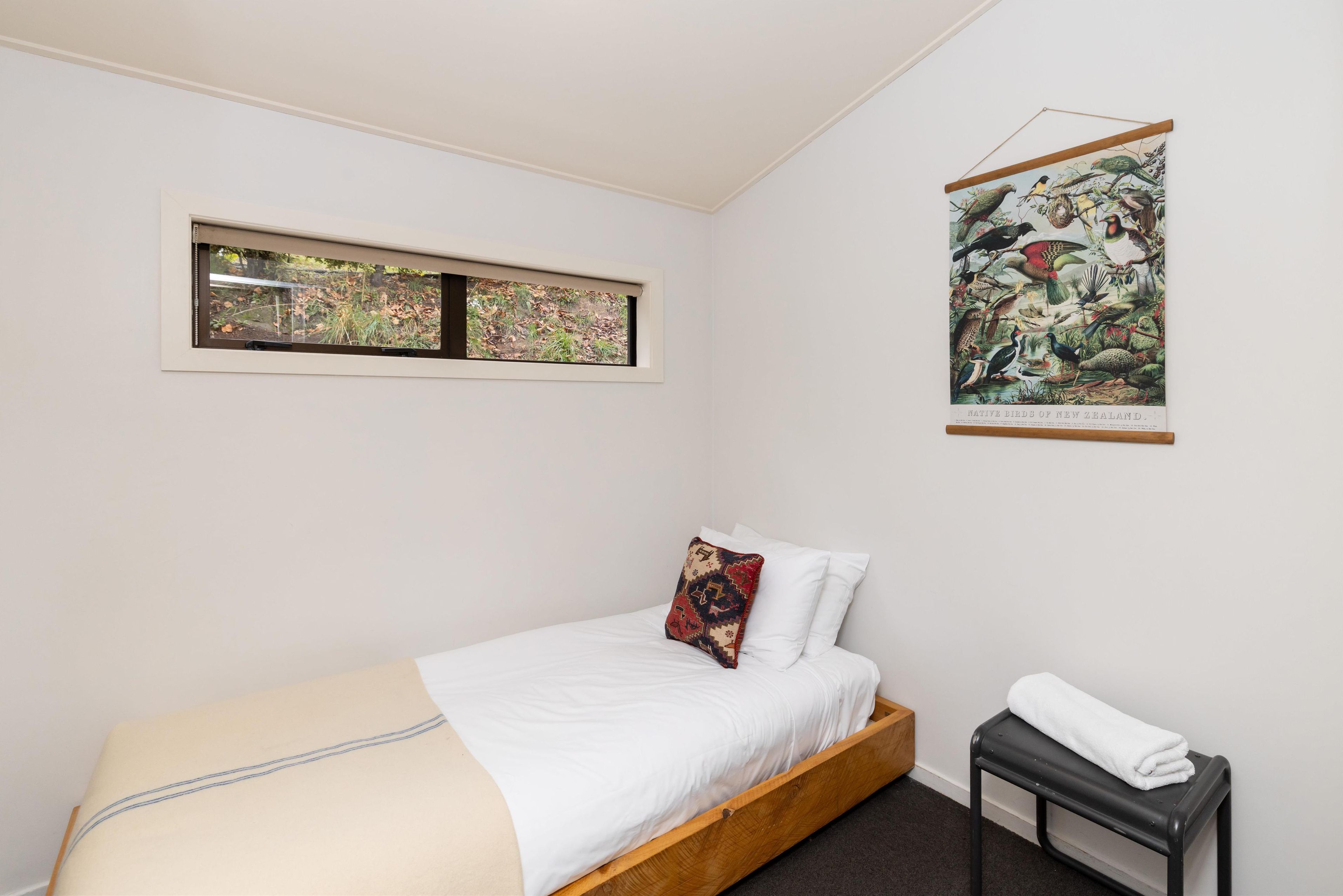 A bedroom with a bed, a window, a wall-mounted picture, and a small table with a towel.