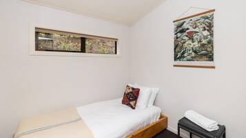 A bedroom with a bed, a window, a wall-mounted picture, and a small table with a towel.