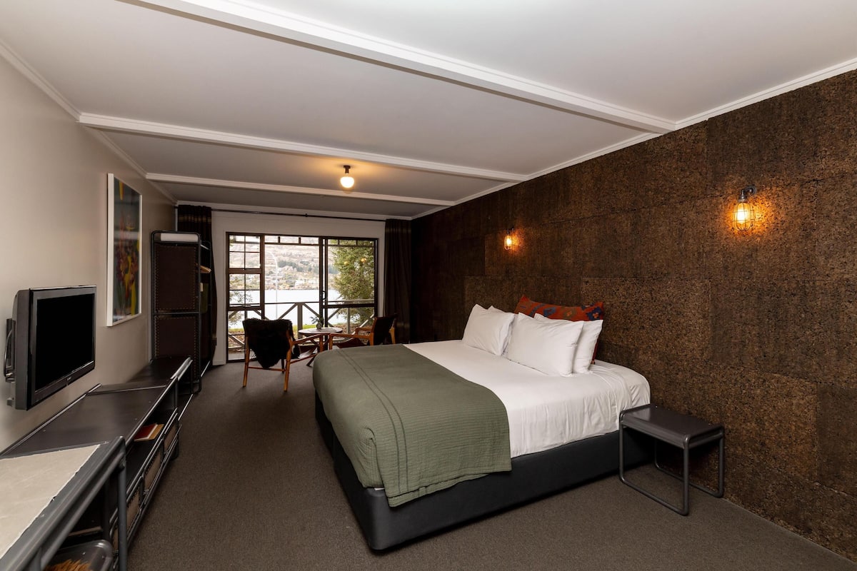 A modern hotel room with a large bed, a TV, a desk, and a view of the outdoors.