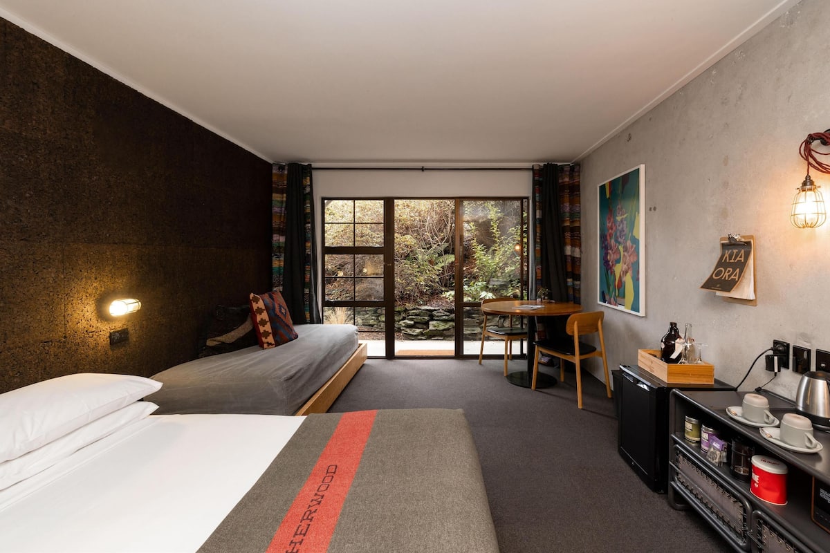 A modern hotel room with a bed, a small table, a desk with a coffee machine, and a view of the outdoors.