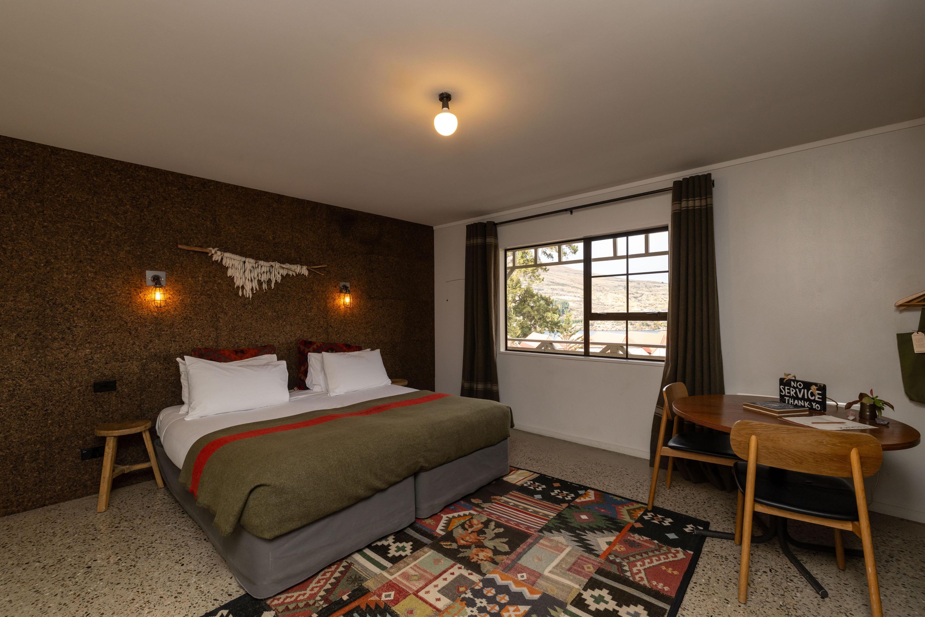 A bedroom with a bed, a desk, a chair, a window, and a wall-mounted light fixture.