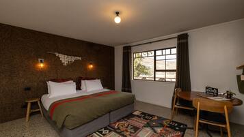 A bedroom with a bed, a desk, a chair, a window, and a wall-mounted light fixture.
