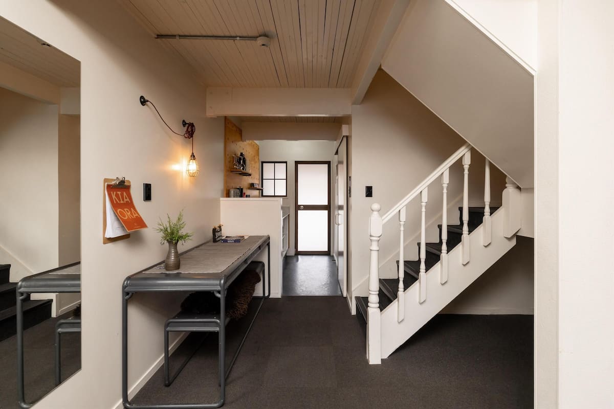 A hallway with a staircase, a desk with a plant, and a wall-mounted light fixture.