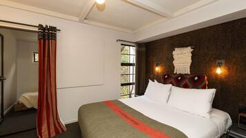 A hotel room with a large bed, a window with a view, a curtain, and a wall-mounted light fixture.