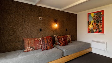 A room with a brown textured wall, a grey sofa with patterned cushions, a wooden platform, and a red and yellow artwork on the wall.