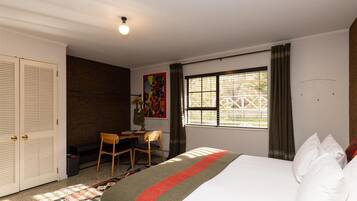 Un dormitorio con cama, escritorio, silla, armario y ventana con cortinas.