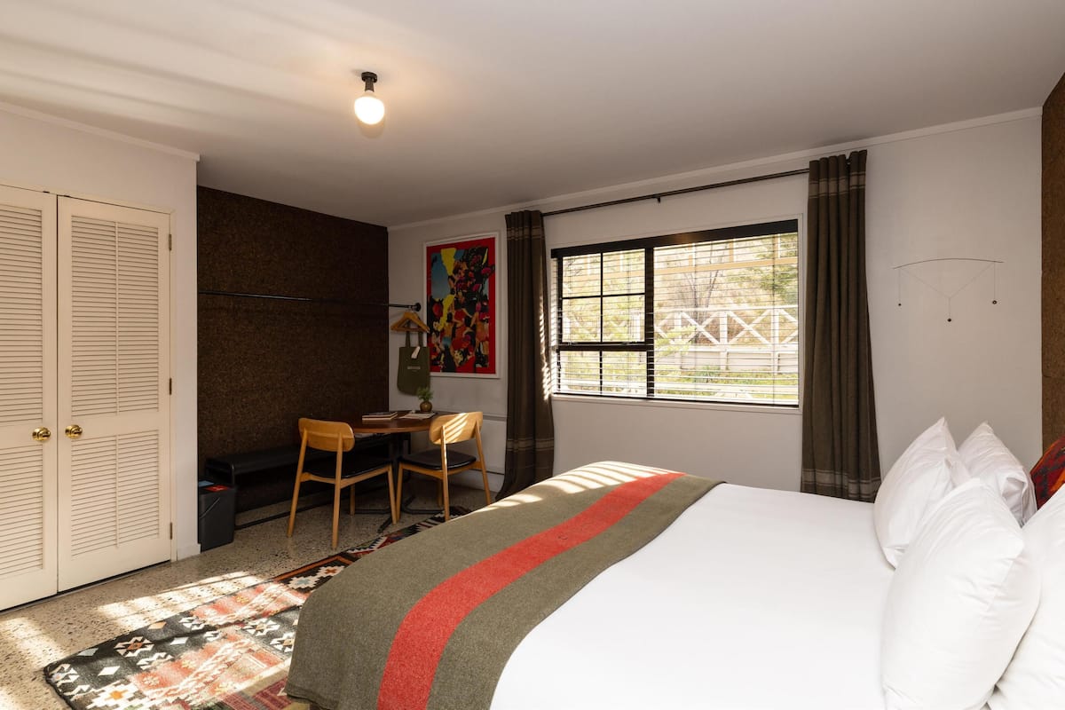 A bedroom with a bed, a desk, a chair, a wardrobe, and a window with curtains.