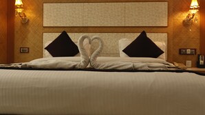Una habitación de hotel con una cama grande, dos almohadas negras, una disposición de toallas con forma de corazón y lámparas fijadas a la pared.