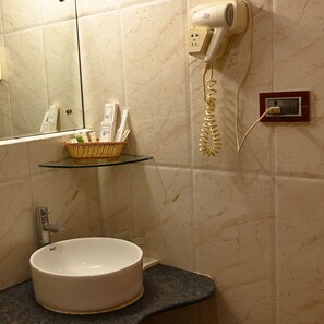 Un baño con un lavabo redondo, un secador de pelo montado en la pared y un estante con artículos de aseo.