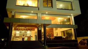 Un hotel de varios pisos con diseño moderno, que cuenta con una entrada destacada con escalones que conducen a la puerta, amplias ventanas en cada planta y un techo plano con un letrero visible en la parte superior.