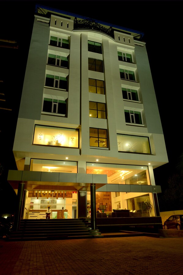 Un hotel de varios pisos con diseño moderno, que cuenta con una entrada destacada con escalones que conducen a la puerta, amplias ventanas en cada planta y un techo plano con un letrero visible en la parte superior.