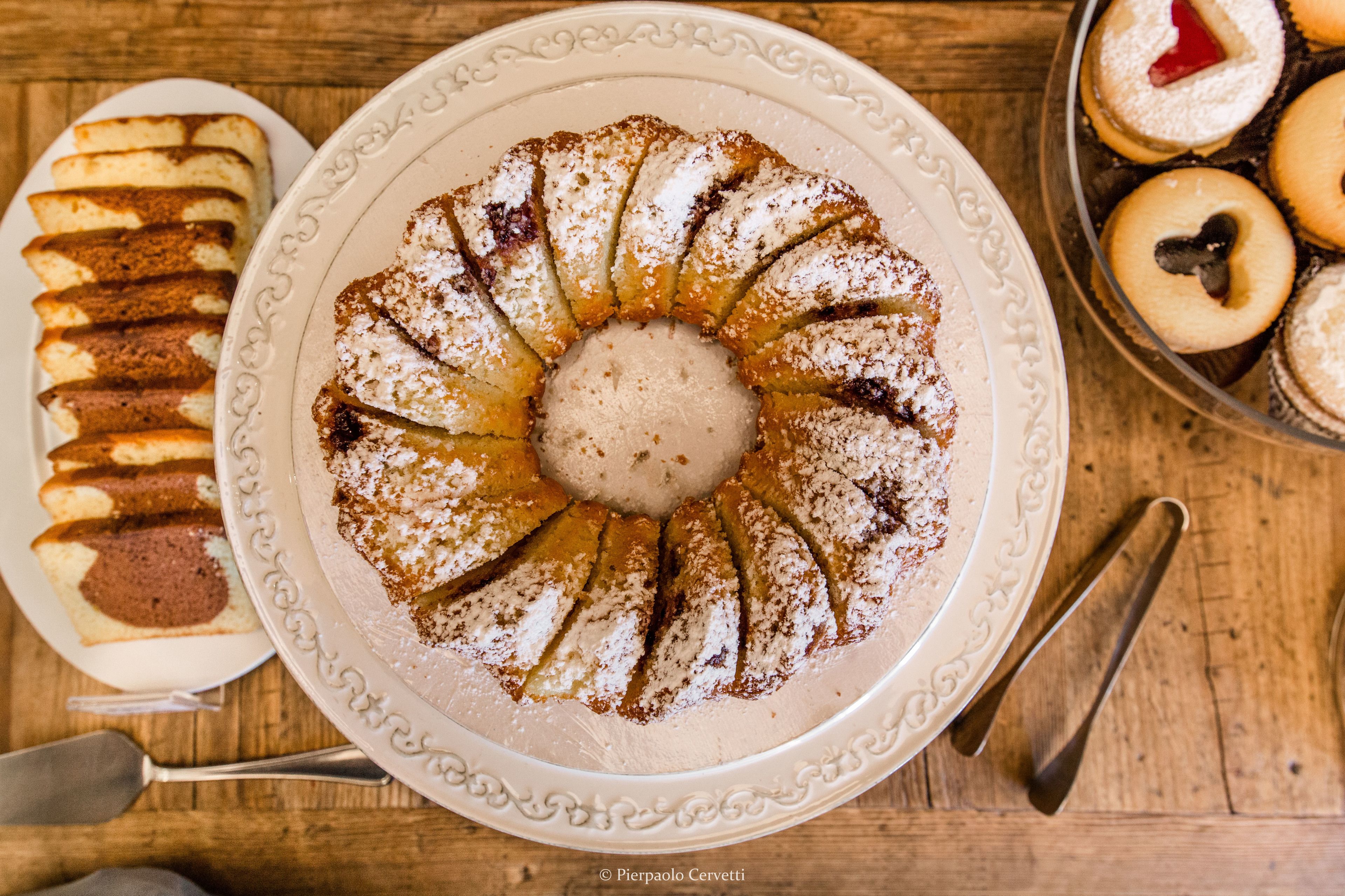 Un piatto dessert con diversi dolci e una torta centrale spolverata di zucchero a velo.