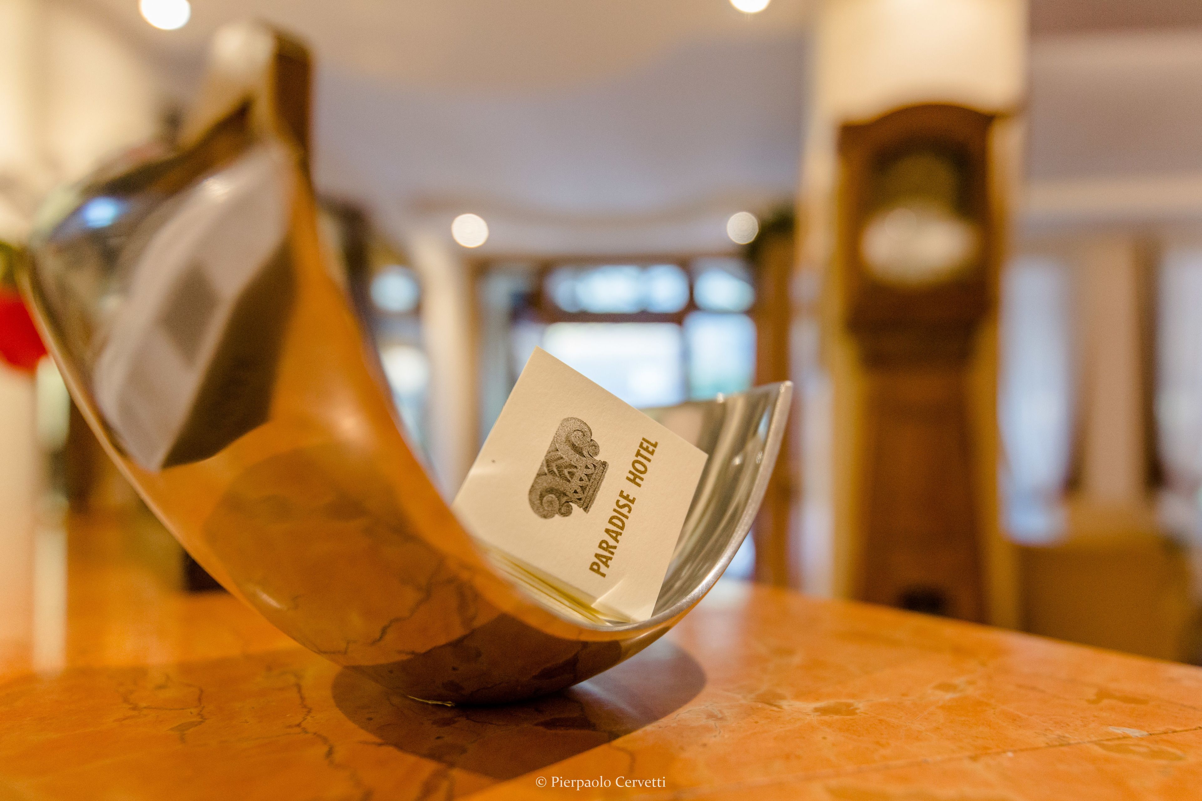 Eine Glasglocke mit einer Karte, auf der 'Paradise Hotel' steht, auf einer Marmorplatte.