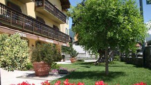 Un hotel con balcón, un jardín de flores rojas y un gran árbol.