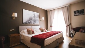 Una habitación de hotel con una cama grande, dos mesitas de noche, un escritorio con silla y una ventana con cortinas.