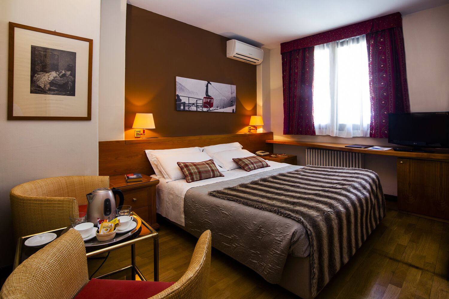 Ein Hotelzimmer mit Bett, Nachttischlampen, Fernseher, Esstisch mit Wasserkocher und Stuhl.