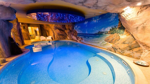 Una amplia piscina interior con un mural de playa tropical, una zona de estar con sillas y un panel de control para las características de la piscina.