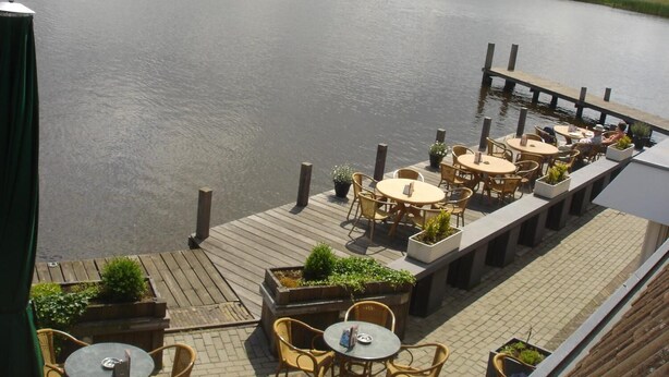 A riverside patio with outdoor seating and a wooden deck overlooking the water. - Hotel Restaurant Ie-Sicht (Oudega)