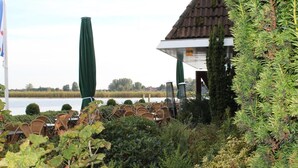 A lakeside outdoor seating area with wicker chairs and a covered pavilion. - Hotel Restaurant Ie-Sicht (Oudega)
