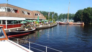 A riverside restaurant with outdoor seating and boats docked nearby. - Hotel Restaurant Ie-Sicht (Oudega)