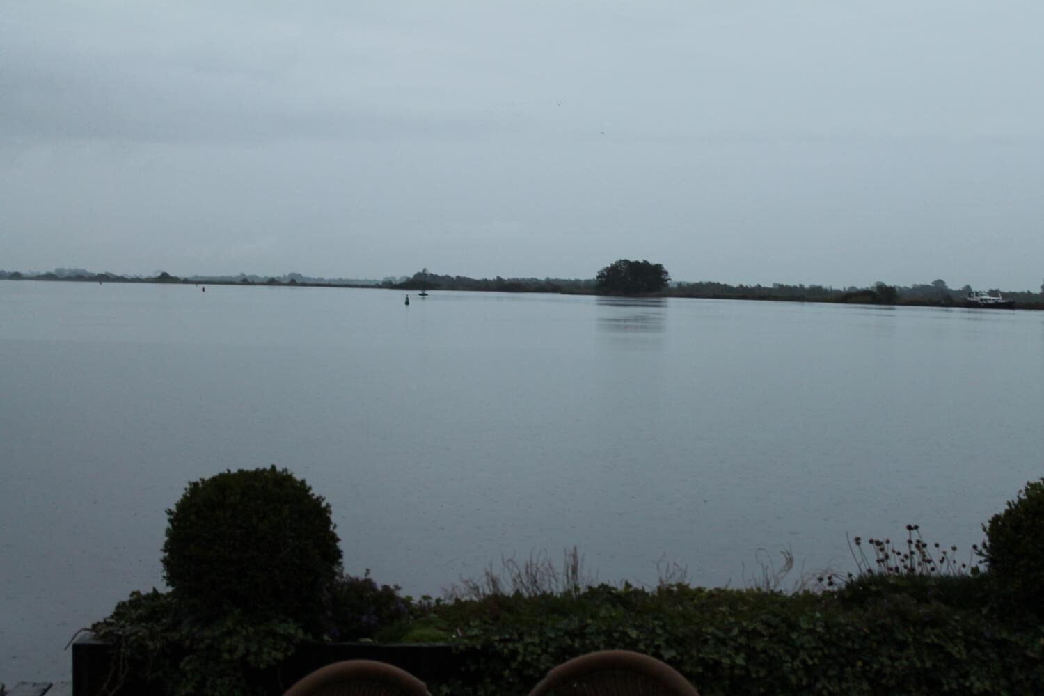 Ein ruhiger See mit einem Baum in der Ferne und einem kleinen Boot.