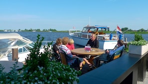 A group of people seated at a table on a boat with a view of the water and other boats in the background. - Hotel Restaurant Ie-Sicht (Oudega)