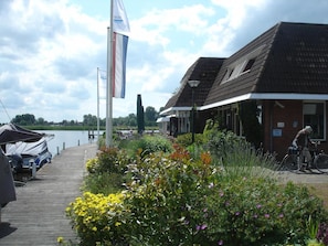 A riverside hotel with a dock, outdoor seating, and a cyclist. - Hotel Restaurant Ie-Sicht (Oudega)