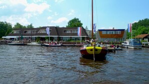 A riverside building with a docked colorful boat in the foreground. - Hotel Restaurant Ie-Sicht (Oudega)