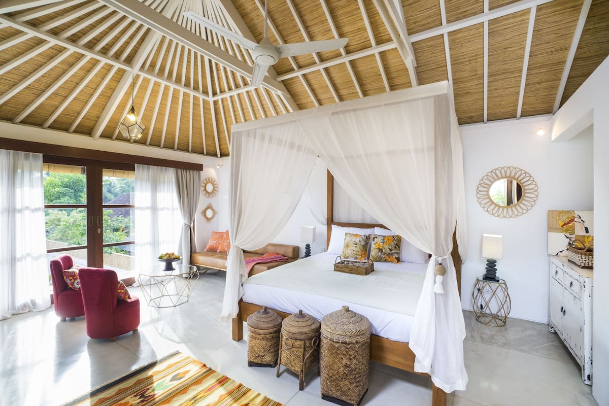 A spacious bedroom with a large bed, a canopy, and a view of greenery outside.