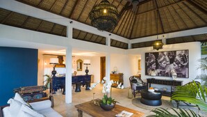 A spacious living area with a high ceiling, a wooden coffee table, a sofa, and a large painting on the wall. - Calma Ubud (Ubud)