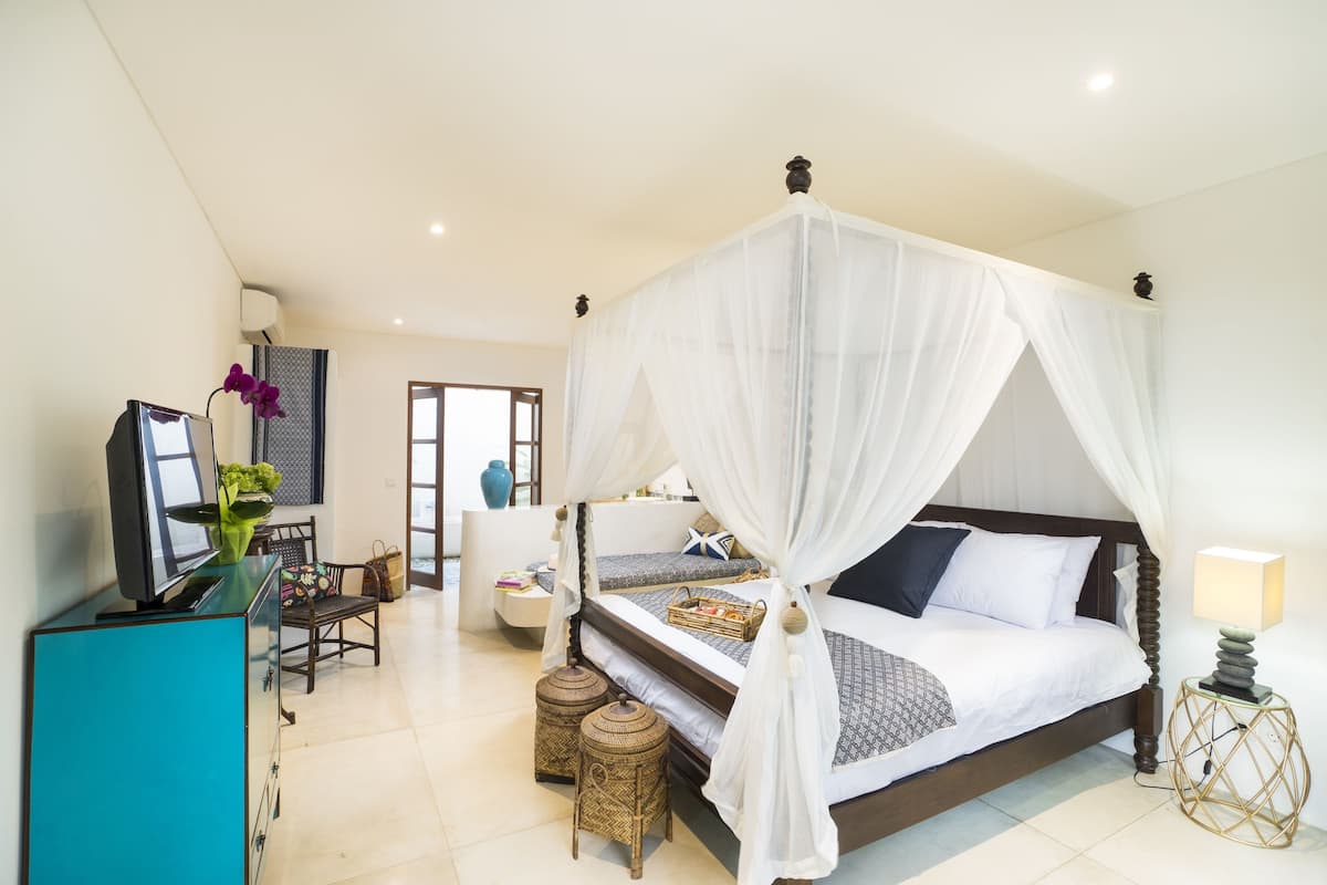 A bedroom with a four-poster bed, a television, a desk with a chair, and wicker side tables.
