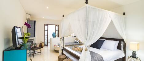 A bedroom with a four-poster bed, a television, a desk with a chair, and wicker side tables.
