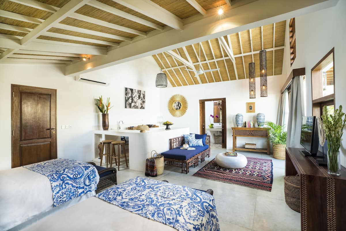 A spacious living area with a high ceiling, a central seating area with a sofa and ottoman, a television, and a dining area with a bar stool.