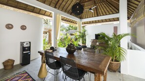 A spacious dining area with a wooden table, black chairs, a water dispenser, and a large potted plant. - Calma Ubud (Ubud)