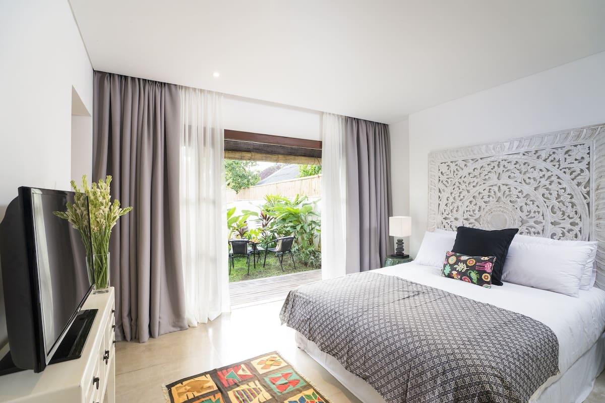 A modern hotel room with a large bed, a television, and a view of the outdoor garden.