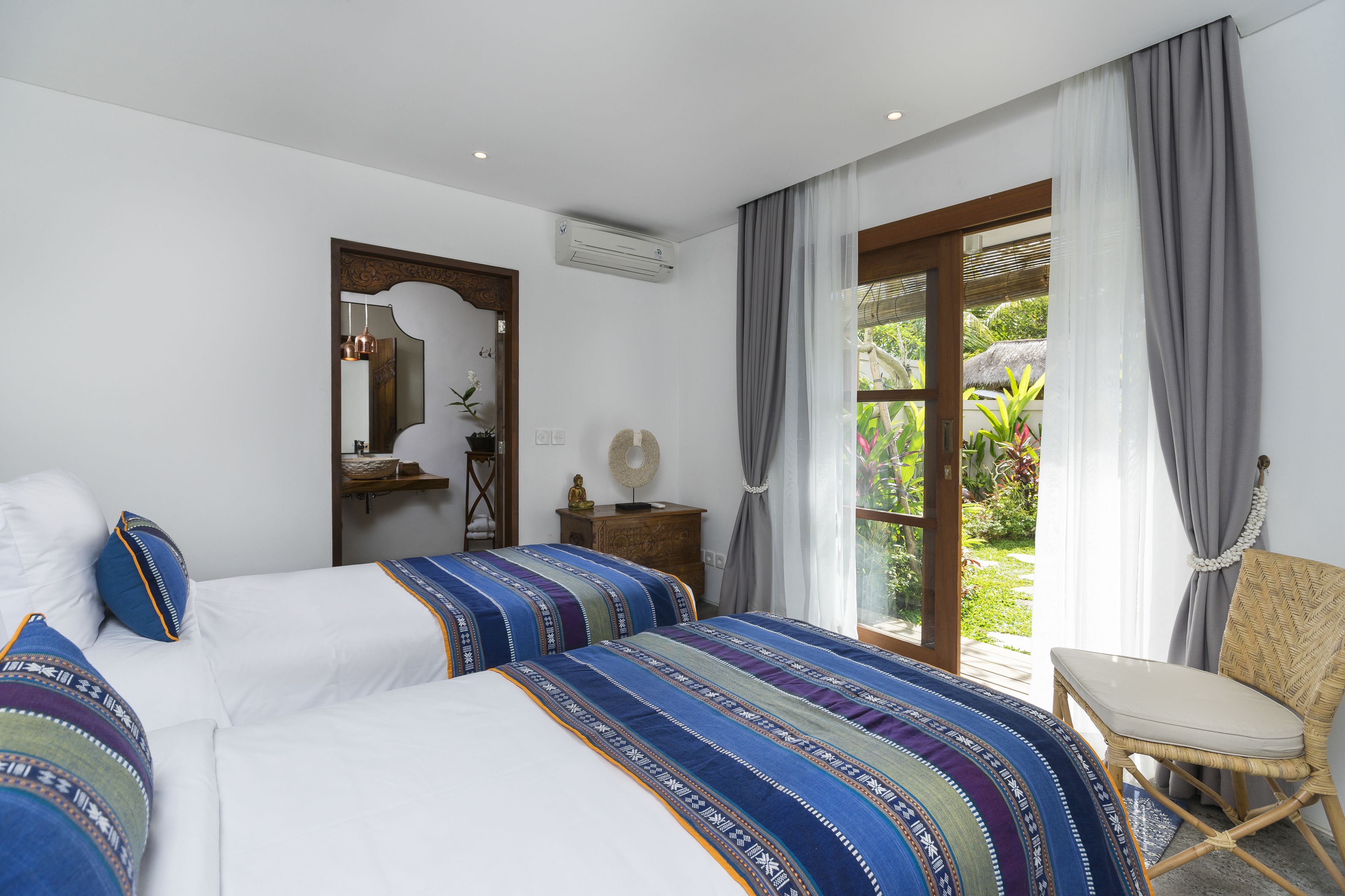 A bedroom with two beds, a chair, a mirror, and a window with curtains.