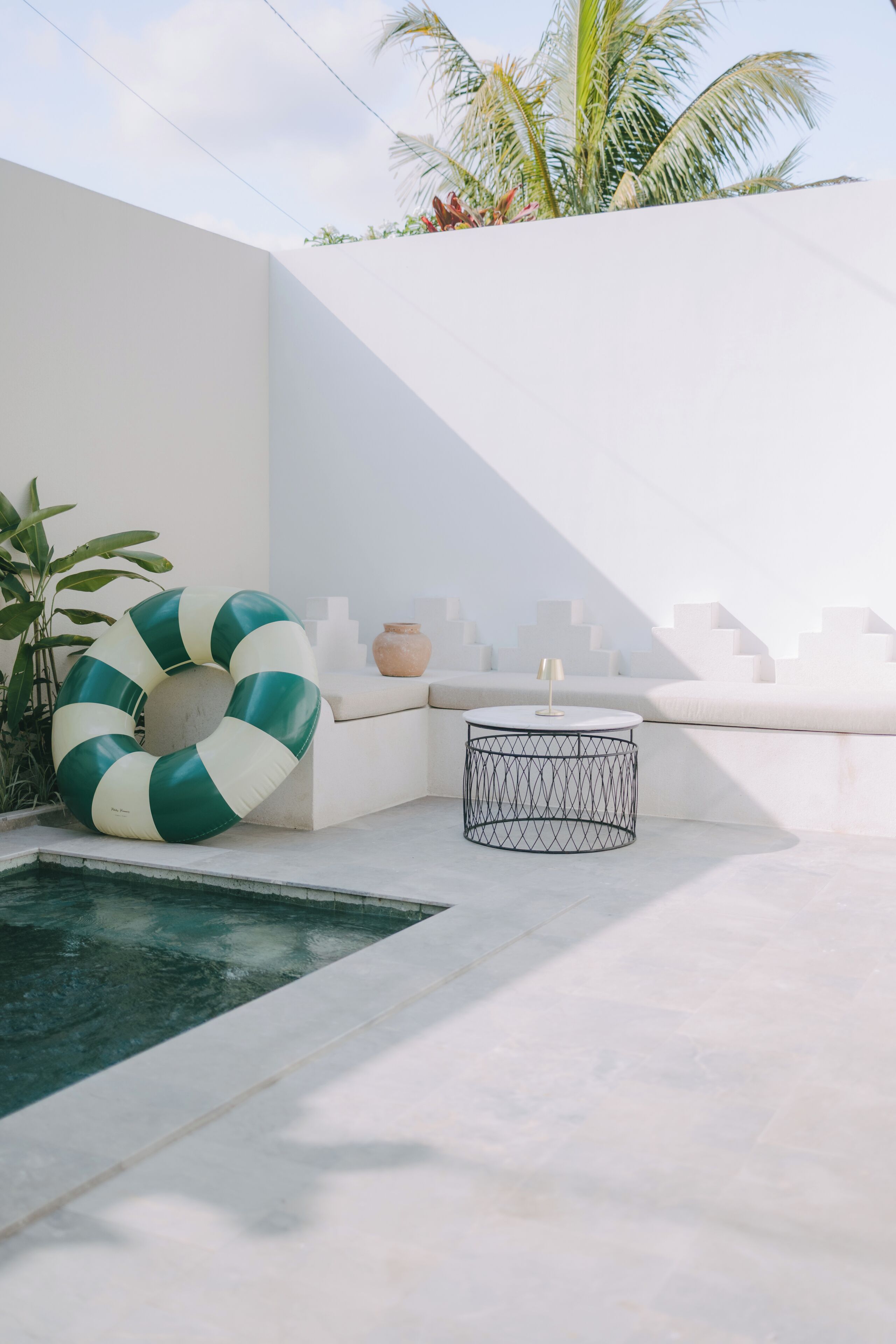 A modern outdoor pool area with a lounge chair, a round table, and a decorative ring.