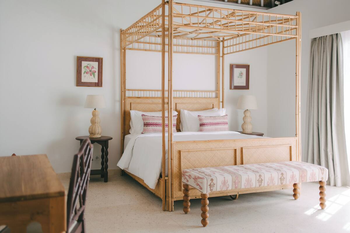 A four-poster bed with a wooden frame and a bench at the foot.