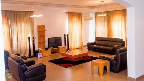 A modern living room with a flat-screen TV, leather sofas, a coffee table, and a wooden TV stand. - The Gilgal Guest House (Lekki)