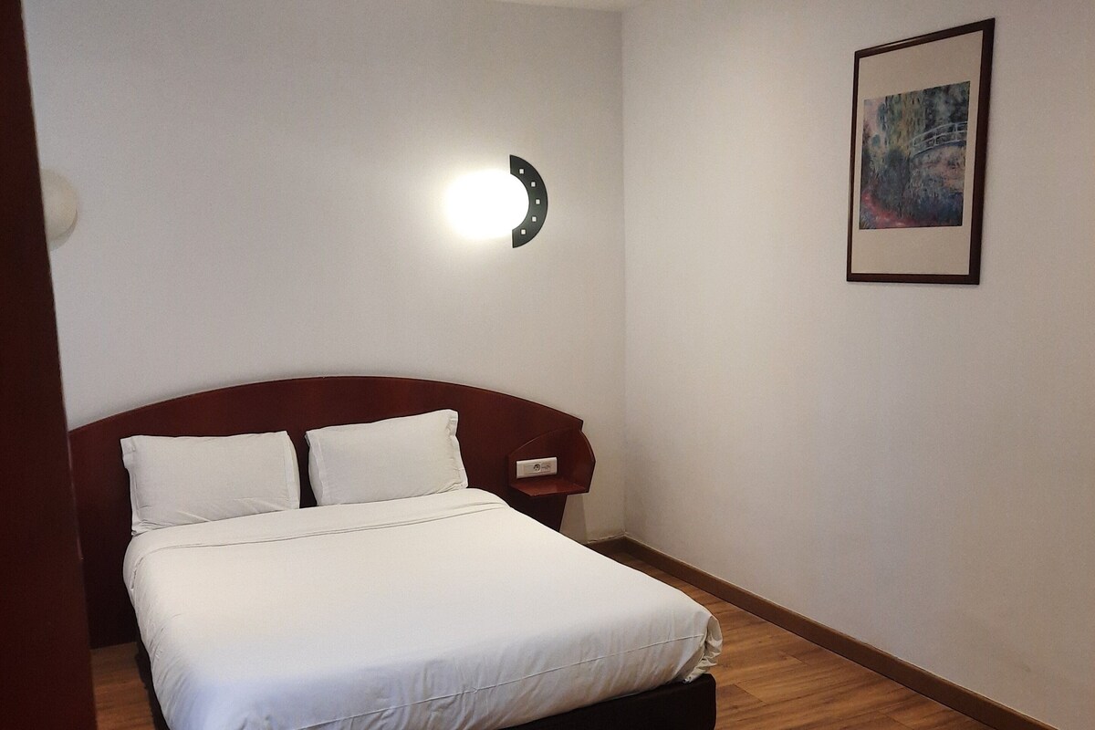 Een slaapkamer met een bed, nachtkastje, een wandlamp en een ingelijste foto.